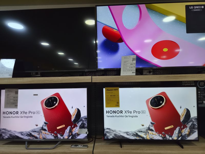 Стенд с телевизорами в магазине электроники: LG QNED и Samsung с ценниками, два Honor-ролика на экранах, слева сверху ещё один телевизор