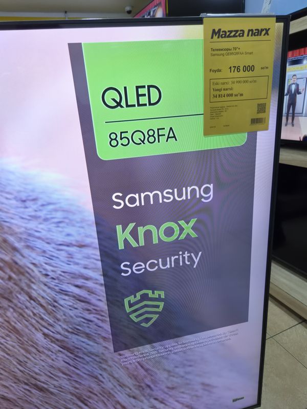 Телевизор Samsung QLED 85" на витрине, на рамке жёлтый акционный ценник «Mazza narx» со старой и новой ценой