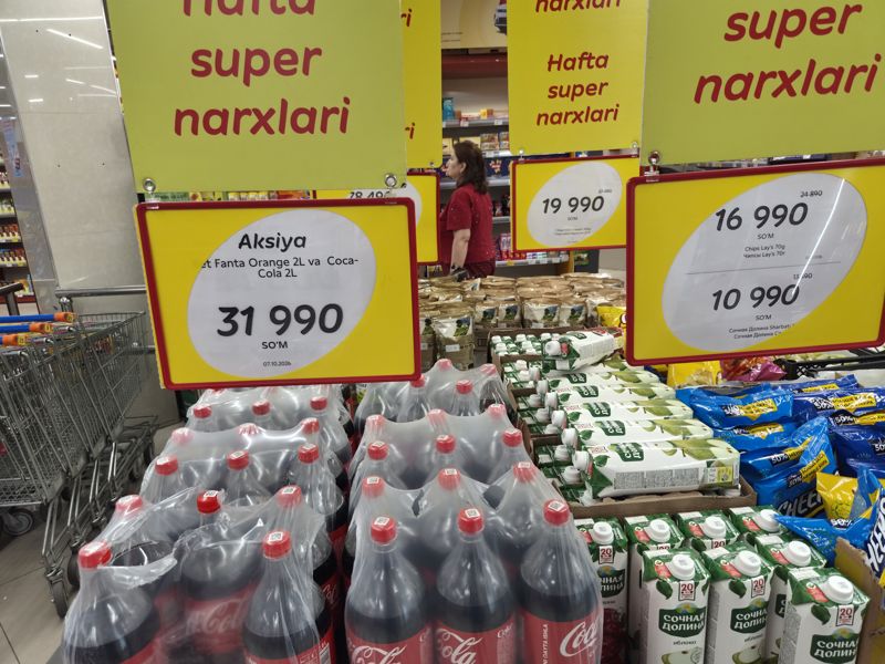 Выкладка у входа в Korzinka под жёлтыми подвесками «Hafta super narxlari»: набор Fanta и Coca-Cola 2 л, мини-круассаны 7 Days, чипсы Lay's и сок Сочная Долина
