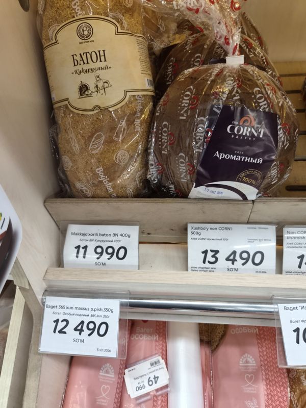 Хлебная полка Korzinka: батон BN кукурузный, хлеб CORN'I Ароматный и багет 365 kun особый подовый с ценниками; на багетах лежит перевёрнутый ценник Nutella