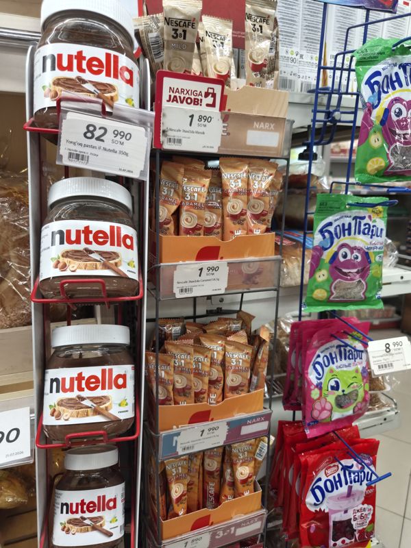 Стойка у хлебного отдела Korzinka: банки Nutella на красном крючковом стеллаже, стаканчики Nescafe 3в1 (классик с красной плашкой «Narxiga javob!», карамель, мягкий) и мармелад Бон Пари справа
