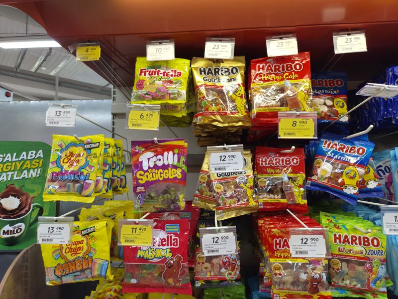 Подвесная выкладка жевательного мармелада в Korzinka: Haribo, Fruit-tella, Fruttella, Chupa Chups, Trolli с белыми и жёлтыми акционными ценниками