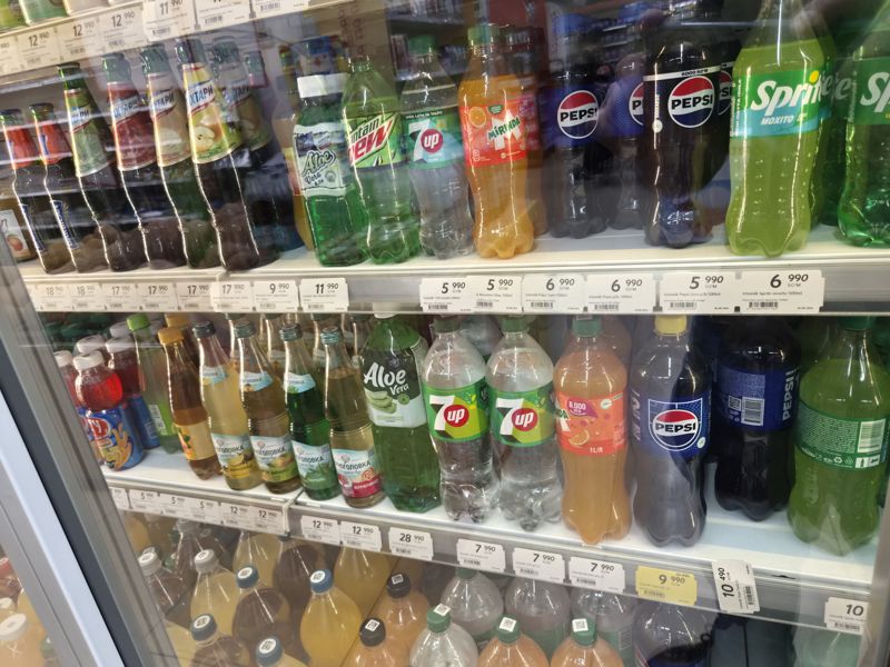 Холодильная витрина с напитками в Korzinka: газировка Pepsi, 7UP, Mirinda, Sprite, Mountain Dew, лимонады Черноголовка и Натахтари; ценники со штрихкодами, один жёлтый акционный