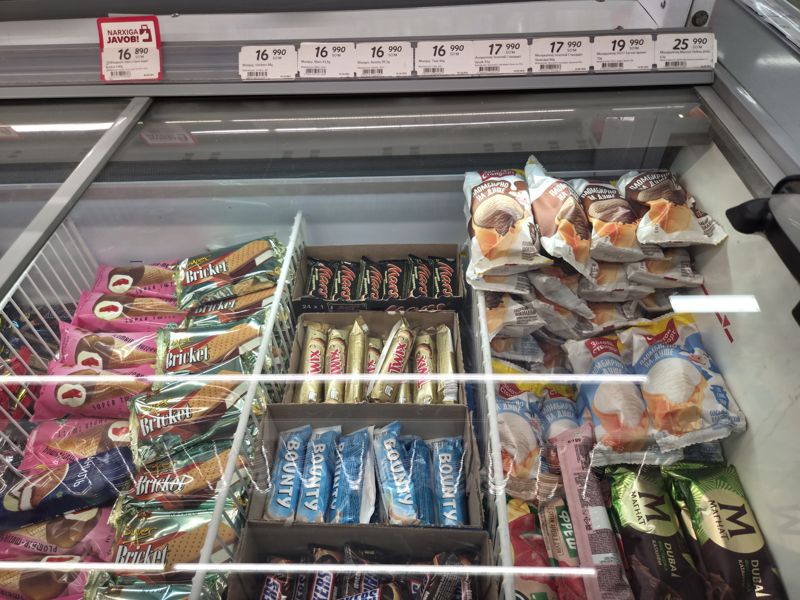 Морозильный ларь с мороженым в Korzinka: Mars, Snickers, Bounty, Twix, Золотой стандарт, Магнат, Super Bricket; ряд ценников со штрихкодами