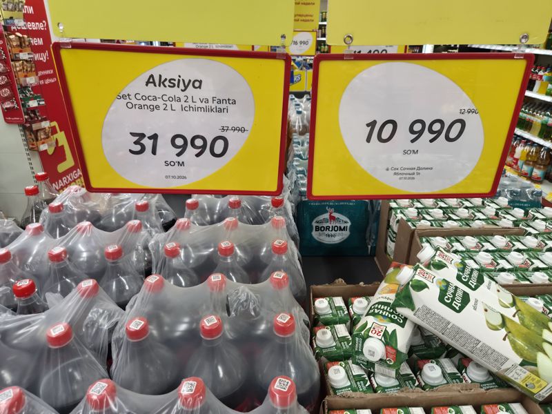 Выкладка колы и сока Сочная долина в Korzinka: ценники набора Coca-Cola 2 л и Fanta Orange 2 л и сока яблочного 1 л