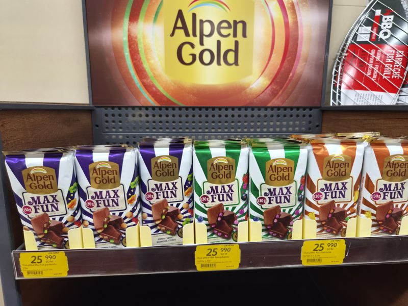Полка с шоколадными плитками Alpen Gold Max Fun 130 г под рекламным плакатом Alpen Gold; три жёлтых акционных ценника с зачёркнутой ценой