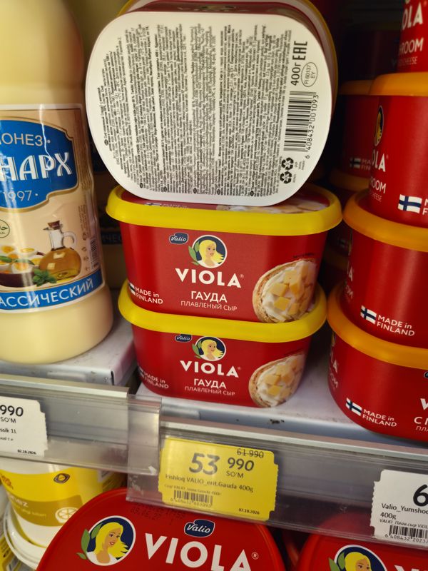 Баночки плавленого сыра Valio Viola Гауда на полке, жёлтый акционный ценник 53 990 сум с зачёркнутой ценой 61 990; крышка одной упаковки с штрихкодом повёрнута к камере