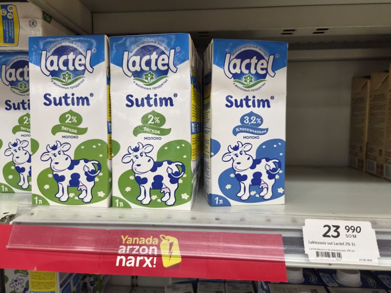 Молоко Lactel Sutim 2% и 3,2% в пакетах по 1 л на полке Korzinka; ценник Lactel безлактозное 2% 1 л, под полкой красная плашка «Yanada arzon narx»