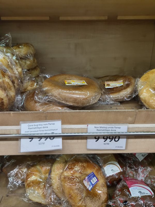 Хлебная полка в Korzinka: патир в плёнке (гречневый и кукурузный) с двумя ценниками Raxmatillaye; ниже хлеб с кунжутом и хлеб CORN'I