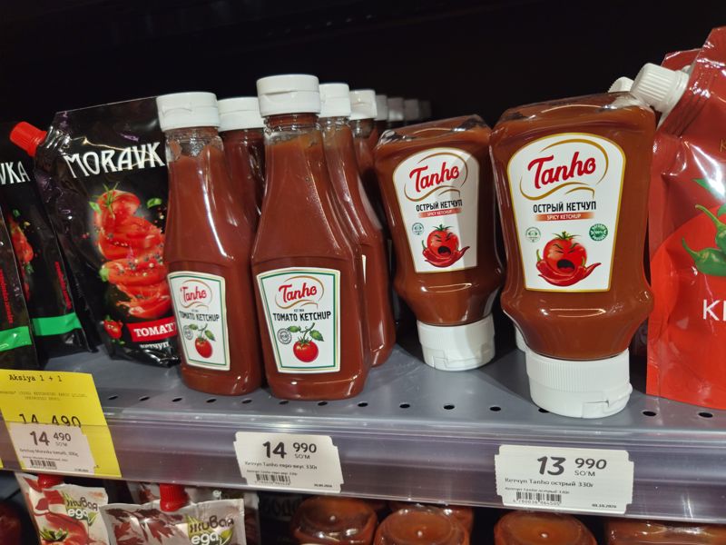 Полка с кетчупом Tanho (евро-вкус, острый), Moravka и пакетами Живая еда; над ценником Moravka жёлтая карточка «Aksiya 1 + 1»