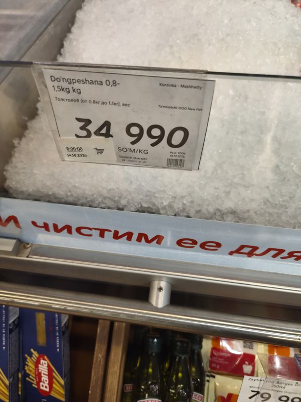 Ценник толстолоба на льду в рыбном отделе Korzinka; снизу полка с макаронами Barilla и оливковым маслом Borges