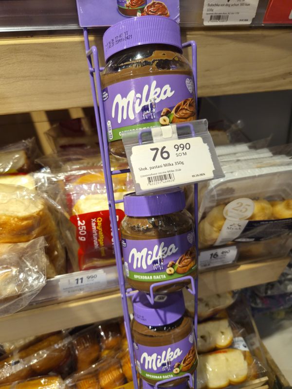 Подвесной стенд с шоколадной пастой Milka (ореховая паста) в отделе выпечки Korzinka, ценник Shok. pastasi Milka 350 г