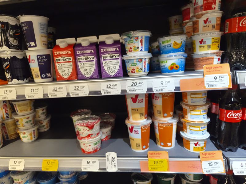Холодильная витрина молочных продуктов Korzinka: кисломолочные напитки, коктейли Exponenta Bio-Skyr, творог и творожная паста, каймак 365 kun, Kamilka, Best; ценники с датой 11.10.2026