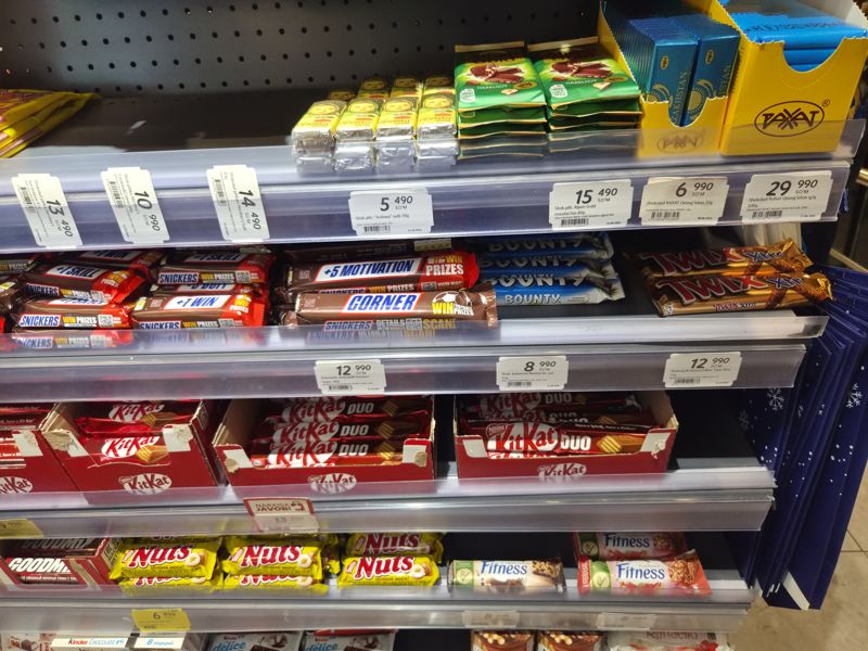 Полки шоколада и батончиков в Korzinka: плитки Алёнка, Alpen Gold, Rahat, Bounty, Twix Xtra, Snickers, KitKat Duo, Nuts; вертикальные ценники Hershey's
