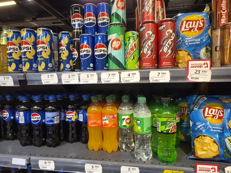 Полка с газированными напитками Pepsi, 7UP, Mountain Dew, Sting, Mirinda в банках и бутылках; справа Lay's сметана и зелень с красной плашкой «Narxiga javob!»