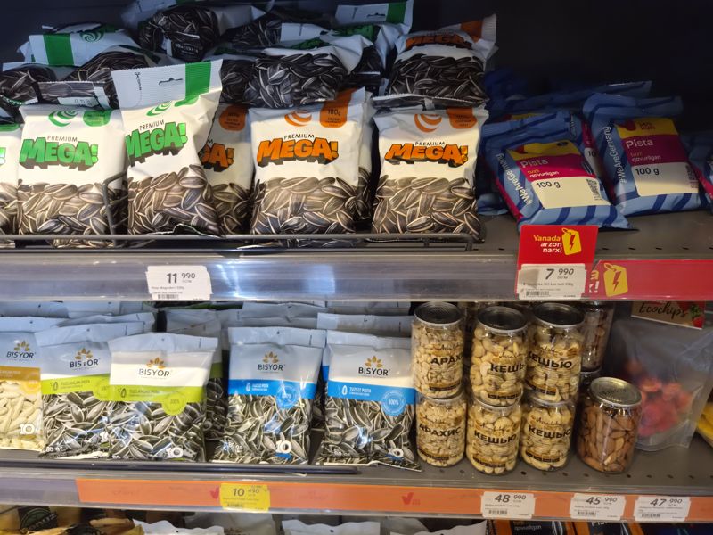 Полки с семечками Mega, 365 kun (плашка «Yanada arzon narx!»), Bisyor и ореховыми банками Assalom nuts; внизу ценники на оранжевой полосе