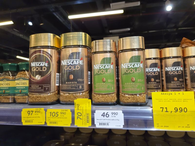 Растворимый кофе Nescafe Gold в стеклянных банках на полке, жёлтые акционные ценники и плакат «Aksiya 1 + 1»