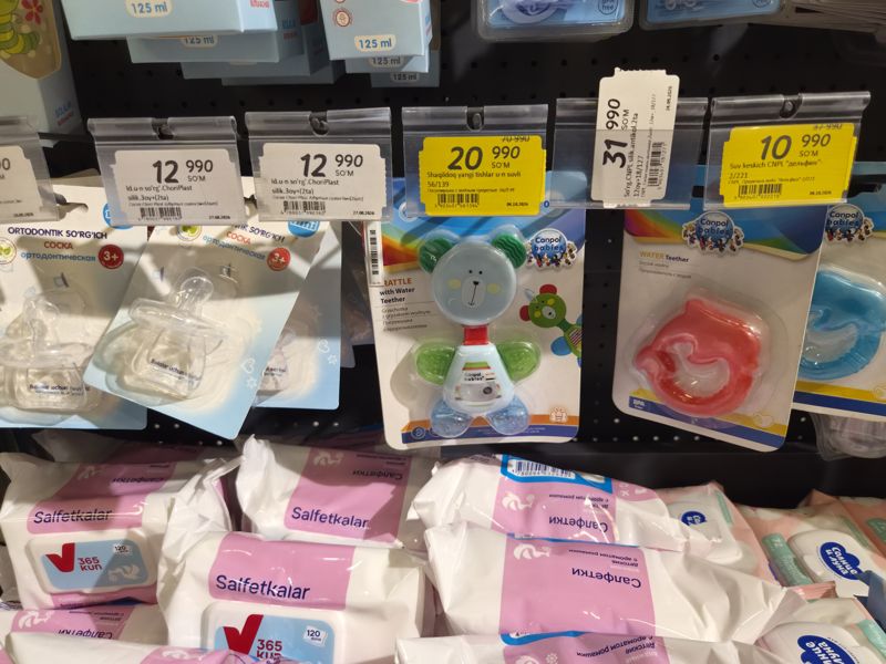Соски Chori Plast, погремушка-прорезыватель и водный прорезыватель Canpol babies на подвесных крючках; детские салфетки «365 kun» внизу; ценники на держателях