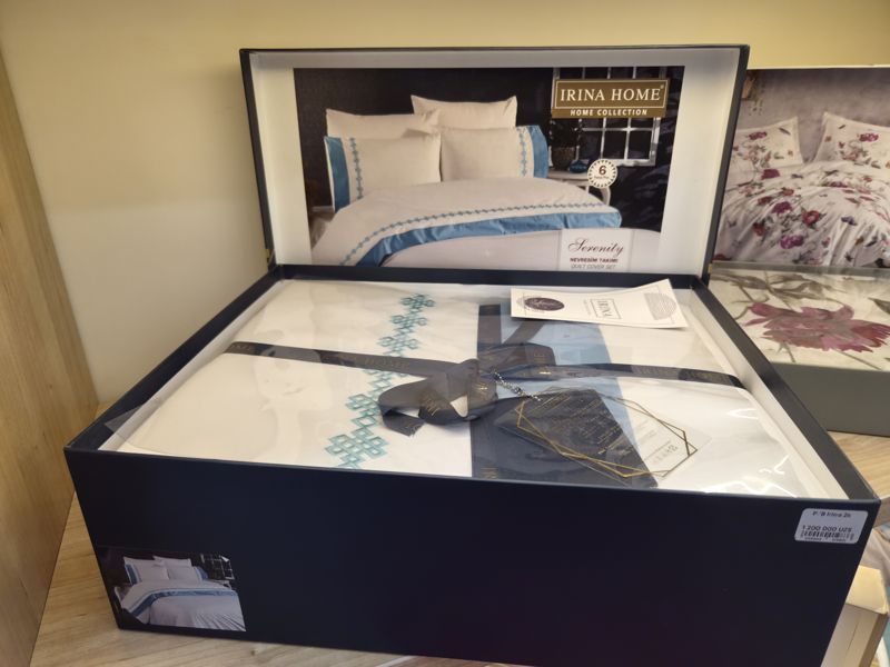 Коробка с комплектом постельного белья Irina Home Serenity (6 предметов, белый с голубой вышивкой) на полке, на борту коробки ценник магазина
