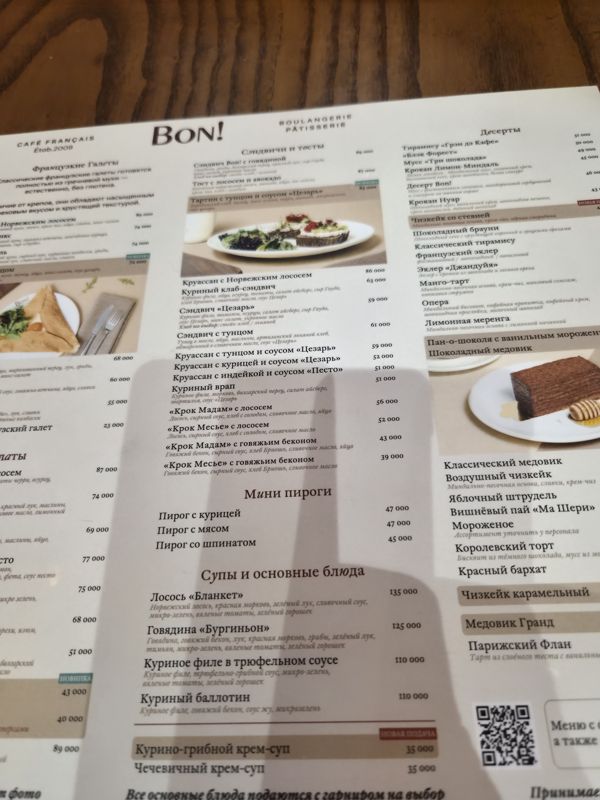 Меню кафе Bon! (еда, лист на столе под углом): сэндвичи и тосты, мини пироги, супы и основные блюда, десерты, левая часть — салаты и галеты; цены в сумах