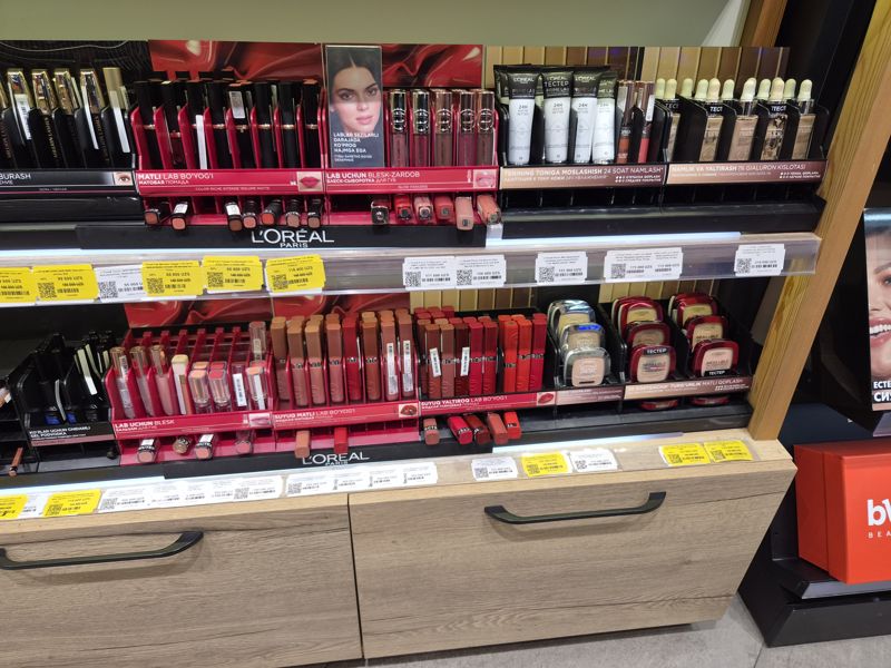 Стенд L'Oréal Paris: помады Color Riche, блески, праймеры, румяна и пудры; ниже шкаф с рядами белых и жёлтых ценников