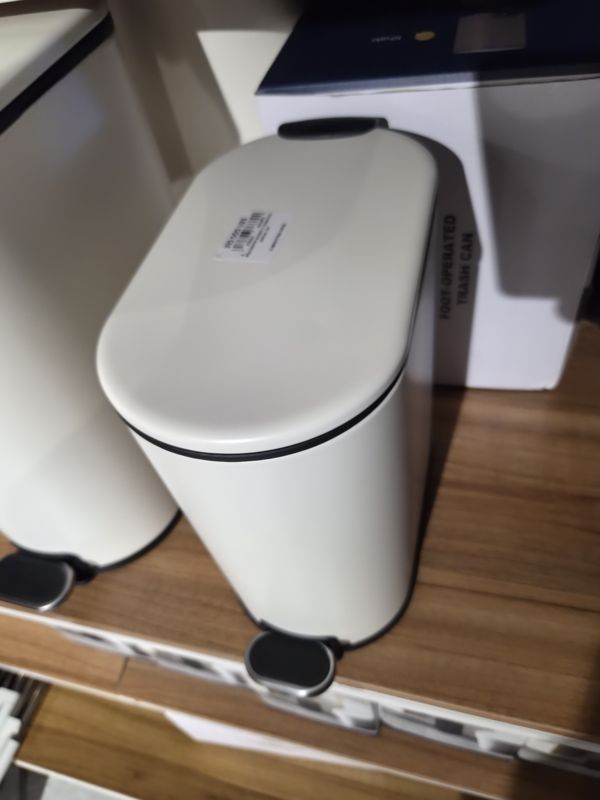 Белое овальное мусорное ведро с педалью на полке, на крышке бирка Scandi Home, на заднем плане коробка Foot-operated trash can