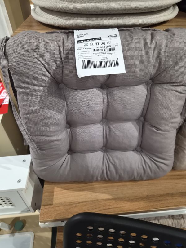 Серая подушка на стул IKEA с завязками и стёганым узором, на ней бирка IKEA и наклейка с ценой Scandi Home; сверху лежат подушки, слева красная плашка SALE