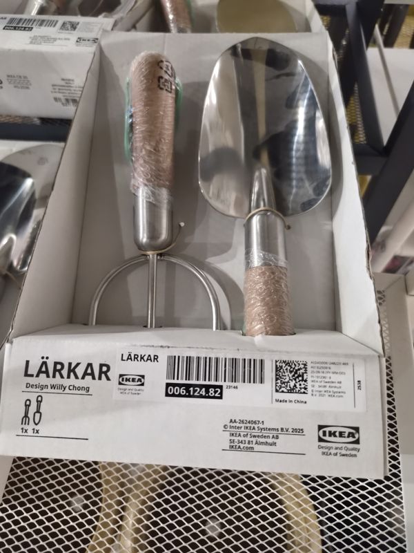 Картонная коробка садового набора IKEA LÄRKAR: вилка-рыхлитель и совок с деревянными ручками, на полке из металлической сетки; слева такие же коробки
