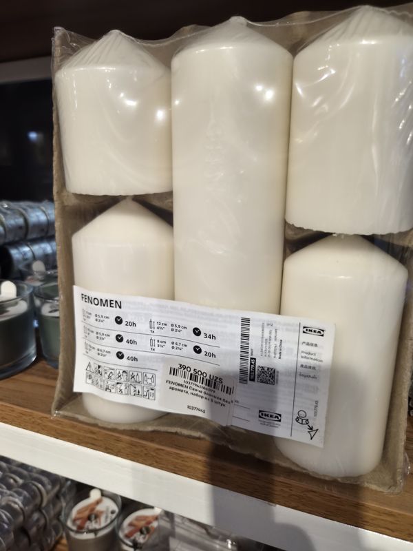 Набор из пяти блочных белых свечей IKEA FENOMEN разной высоты в плёнке на картонной подложке с этикеткой IKEA и наклейкой цены Scandi Home; на полках ниже свечи в стаканах