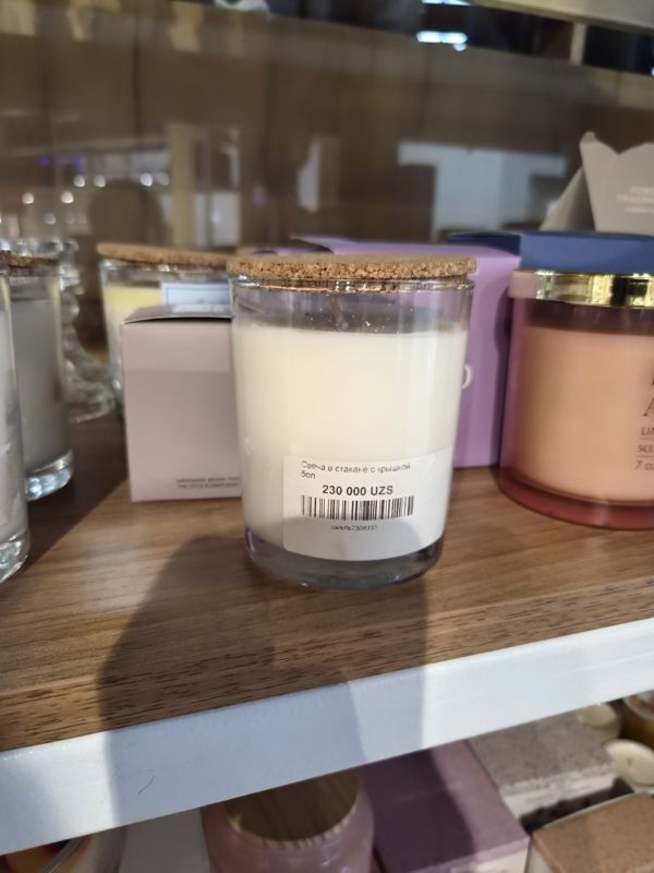 Свеча в стеклянном стакане с пробковой крышкой с наклейкой цены Scandi Home; рядом коробки и другие свечи