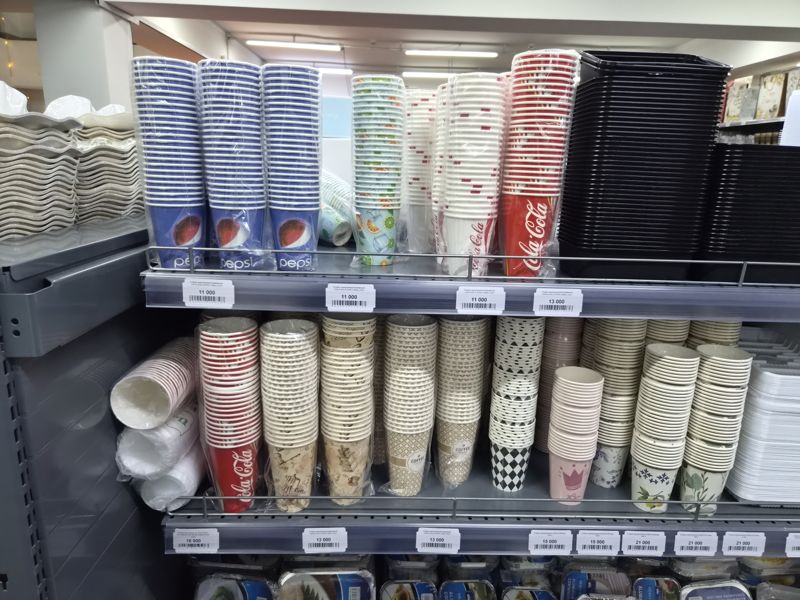 Стеллаж с одноразовыми бумажными стаканами (Pepsi, Coca-Cola, кофейные, цветные) и чёрными пластиковыми контейнерами, ценники 11 000–21 000