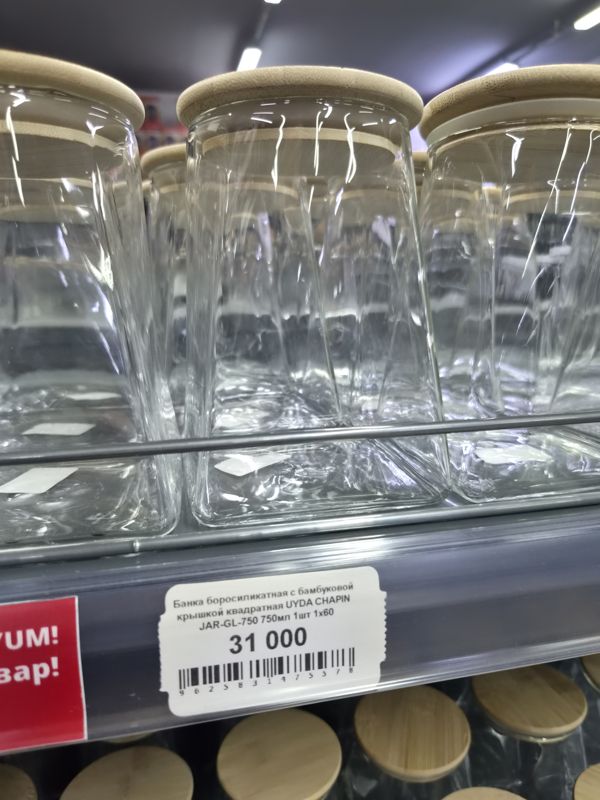 Квадратные стеклянные банки с бамбуковыми крышками на полке, ниже ценник; слева край красной плашки