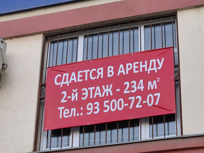 Красный баннер «Сдаётся в аренду, 2-й этаж, 234 м²» на окне с решёткой на фасаде здания