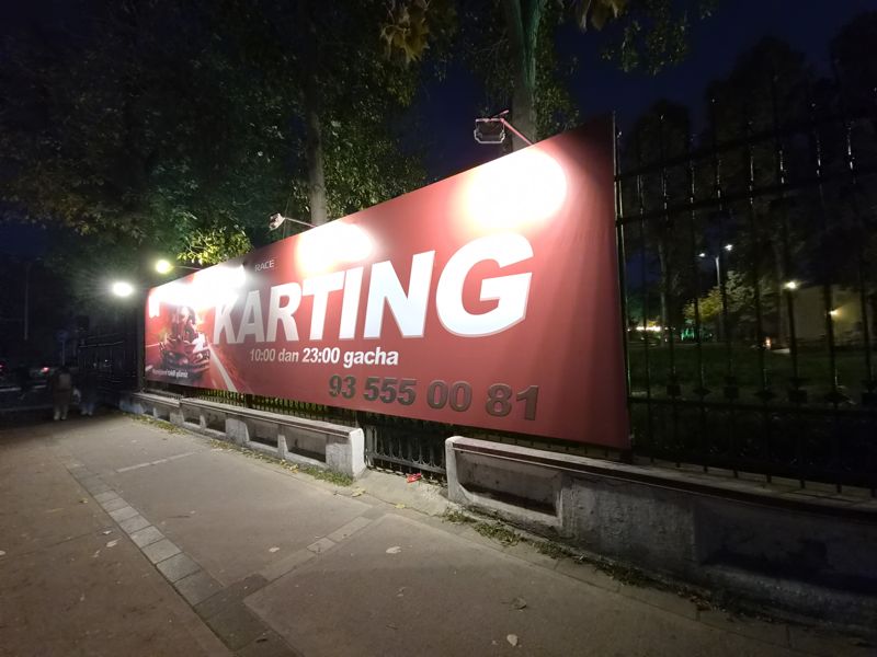 Ночной щит «Karting» Alpine X Race на ограде парка: 10:00–23:00 и телефон; слева вдали прохожие со спины