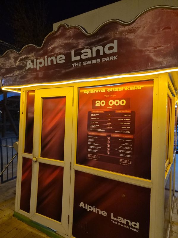 Будка аттракциона «Aylanma chashkalar» (Tea Cups) под вывеской Alpine Land The Swiss Park, табличка с ценой 20 000 сум и правилами